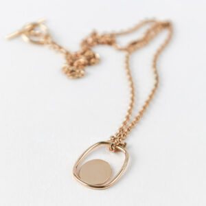 Collier doré présenté sur une pierre blanche poreuse.